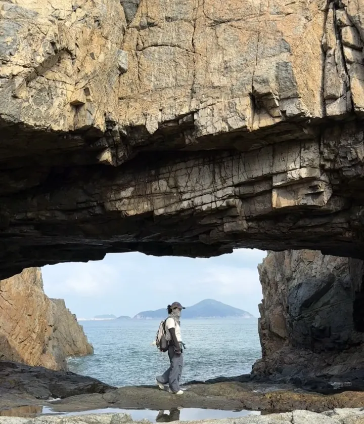 A photograph taken inside a sea cave, looking out through the opening at the water and a distant island